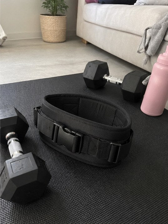 Ceinture Ergolift noire posée sur un tapis de sport avec des haltères